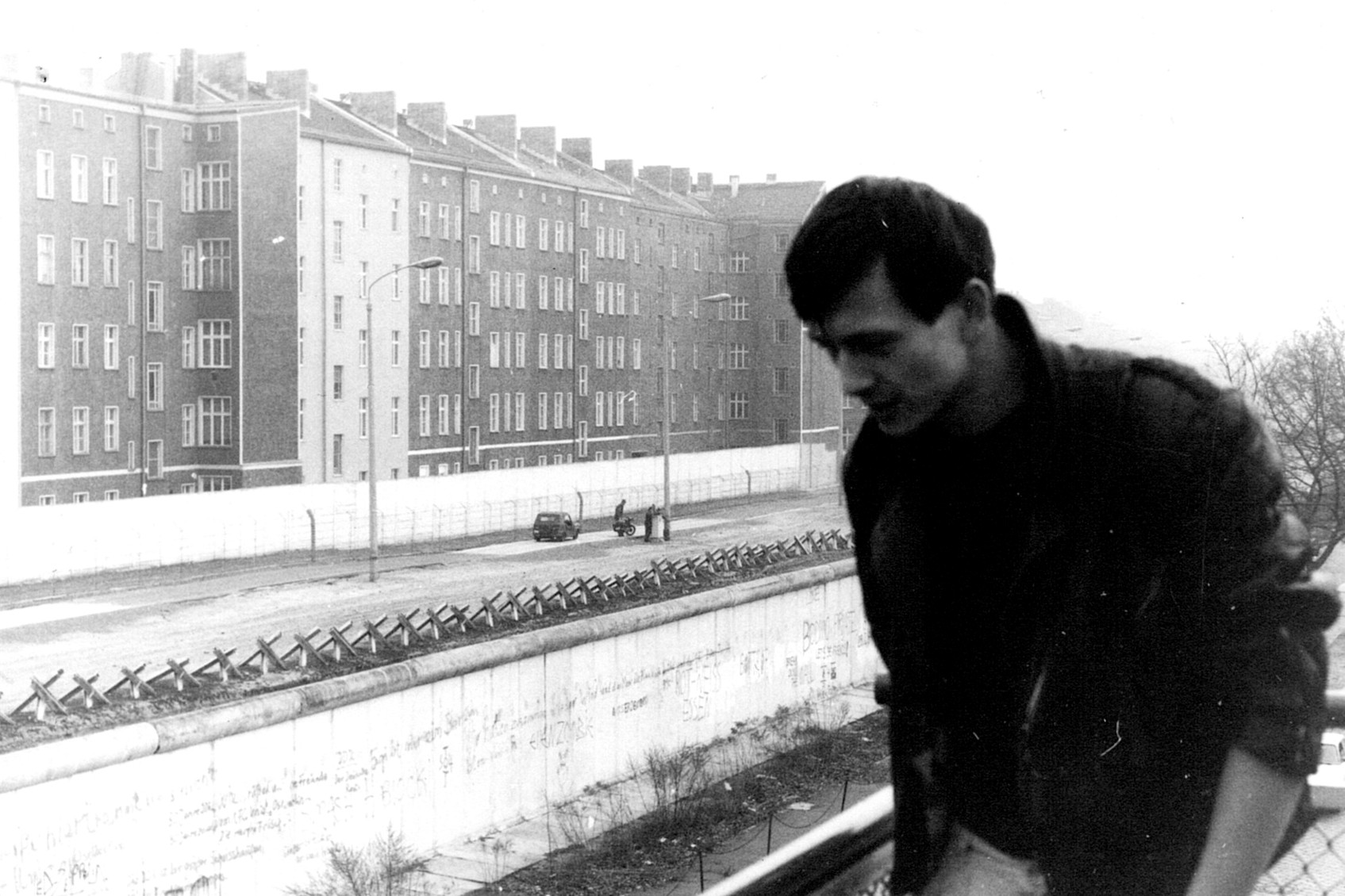 Schwarz-wei&szlig; Foto eines Mannes der &uuml;ber den Grenzstreifen in Berlin schaut.
